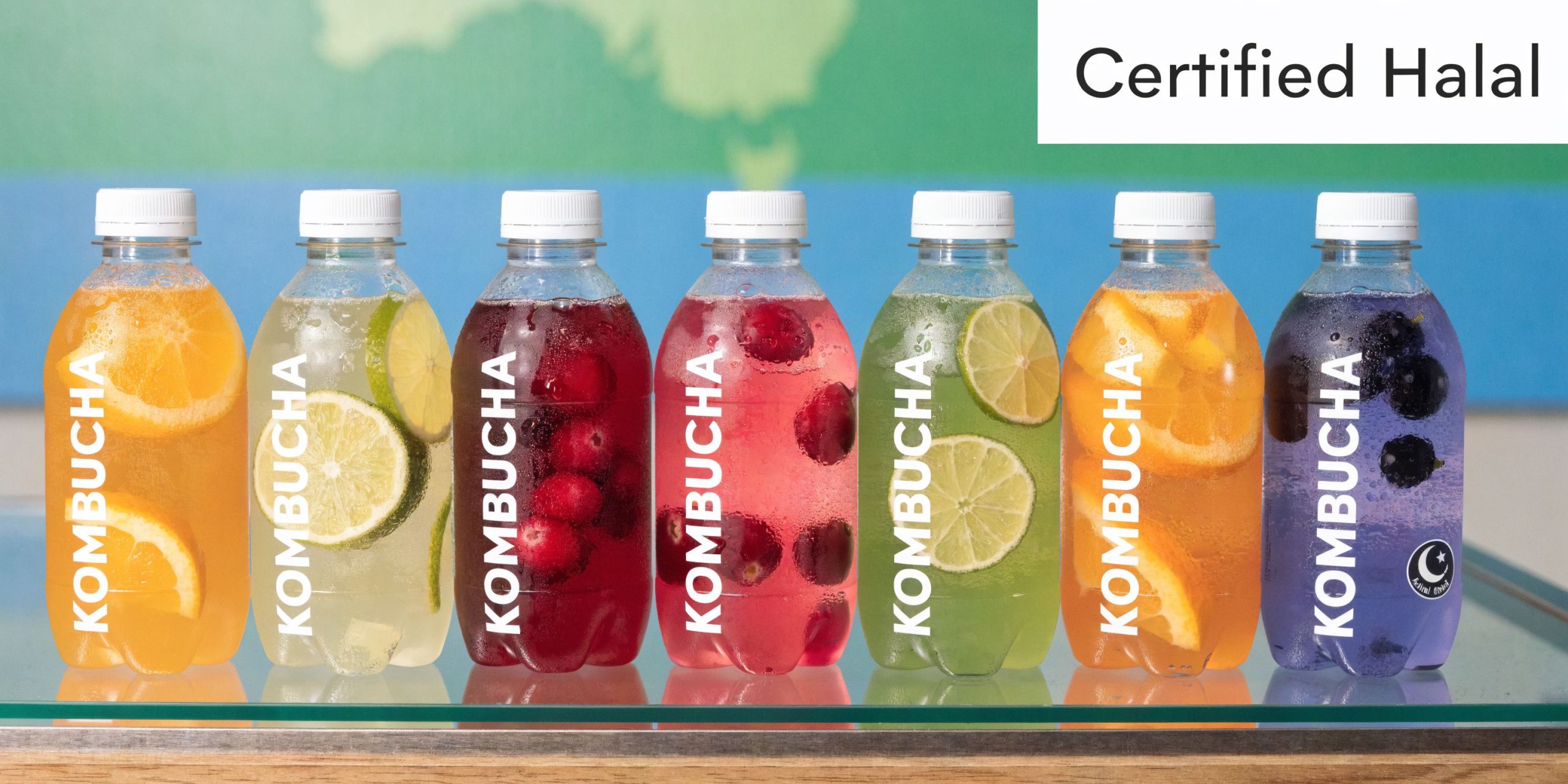A line of seven colorful bottles of kombucha featuring various fruit infusions and a Certified Halal seal.