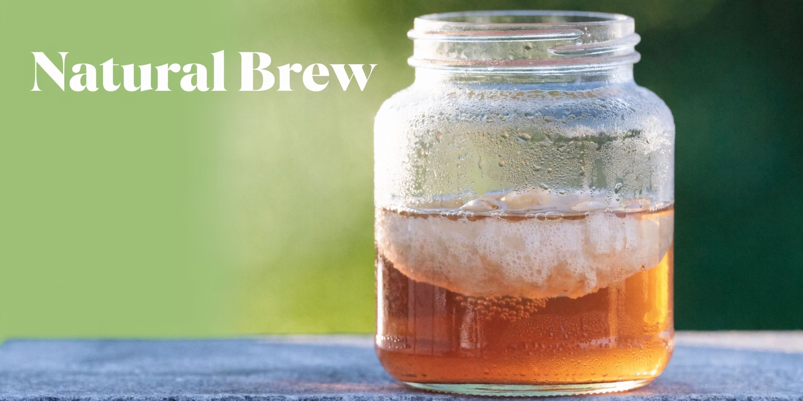 A glass jar containing home-brewed kombucha with a visible scoby floating in the amber-colored liquid.