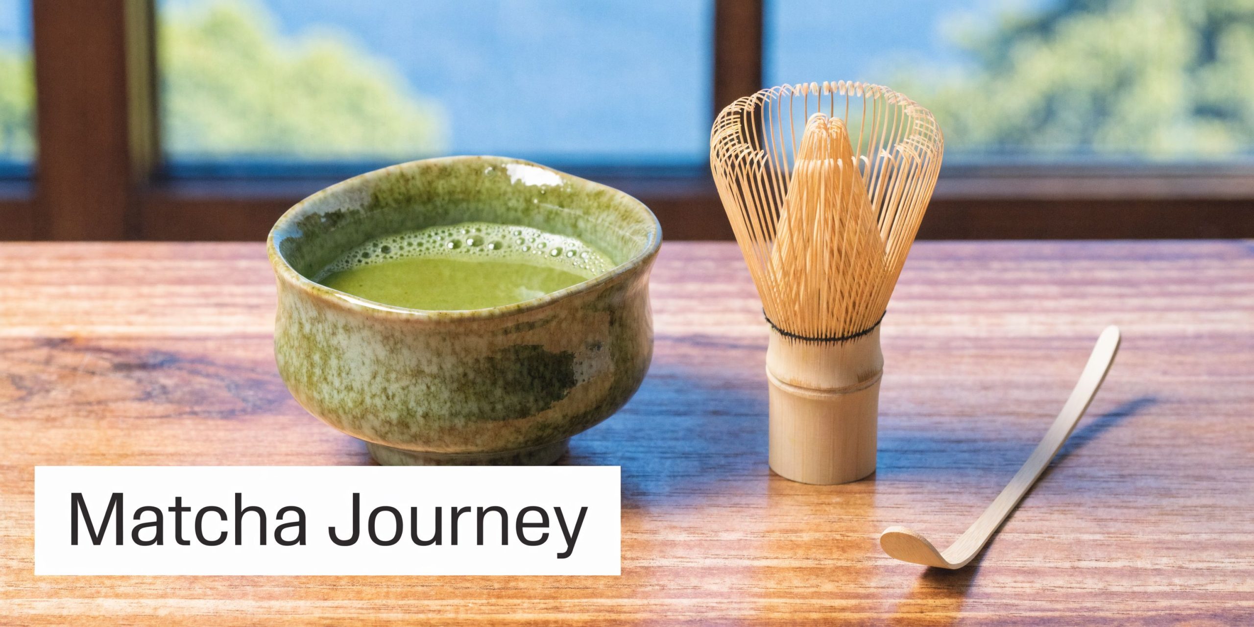 A cup of green matcha tea next to a traditional bamboo whisk and tea scoop on wood.