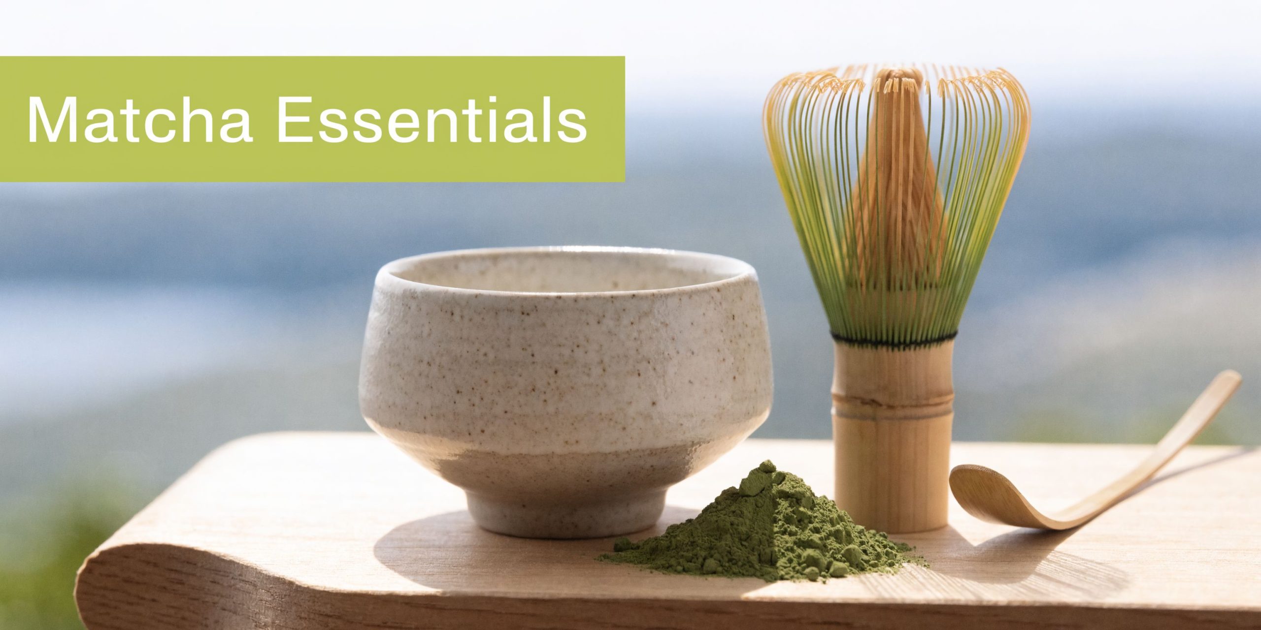 A ceramic bowl, bamboo whisk, and matcha powder on a wooden surface with Matcha Essentials text.