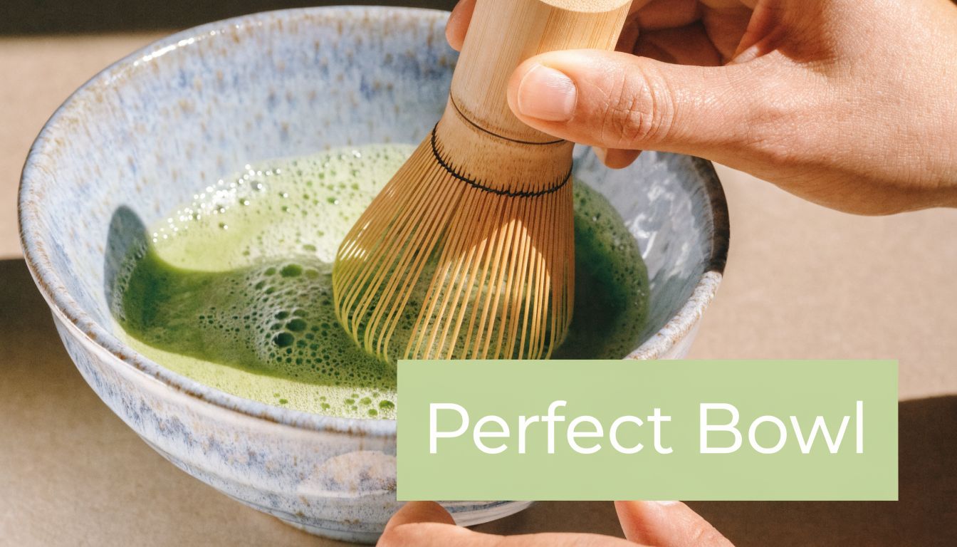 A close-up view of a person using a bamboo whisk to mix green matcha tea in a bowl.