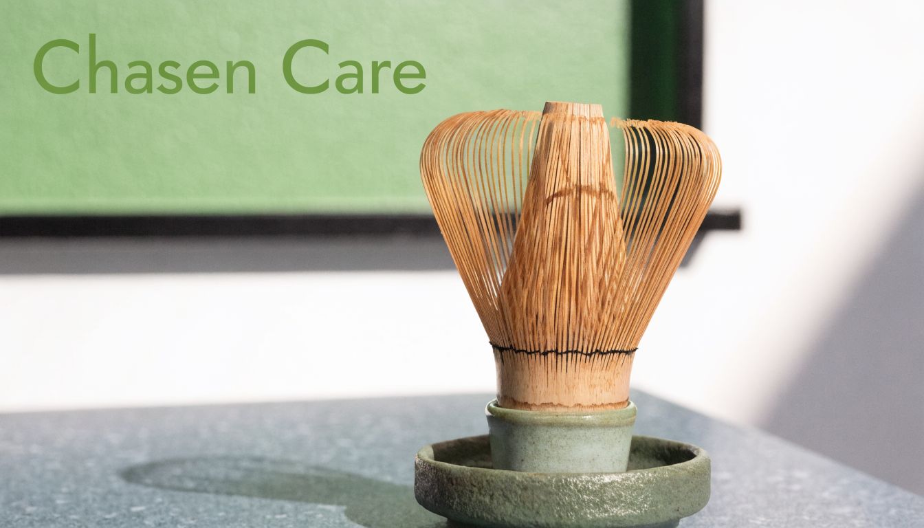 A bamboo matcha tea whisk resting upright in a ceramic holder on a textured surface.