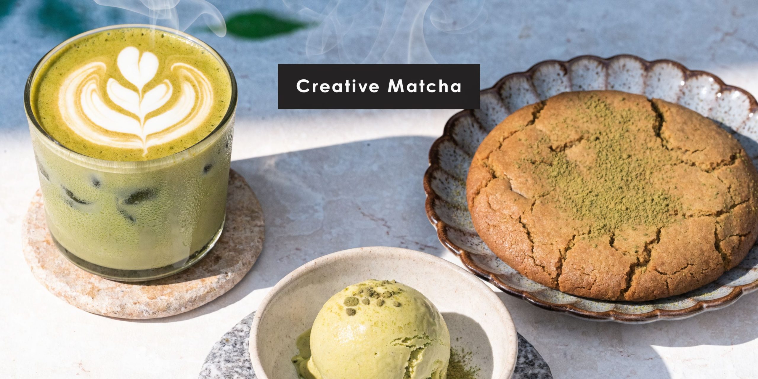 A glass of matcha latte, a matcha ice cream scoop, and a matcha cookie on a table.