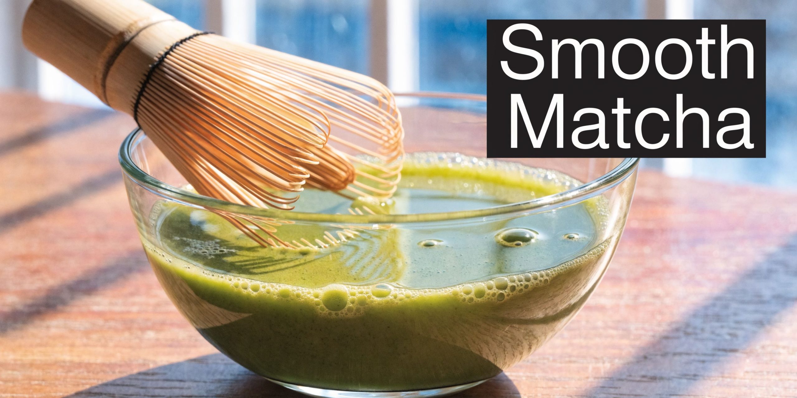 A wooden bamboo tea whisk inside a glass bowl filled with freshly prepared vibrant green matcha tea.