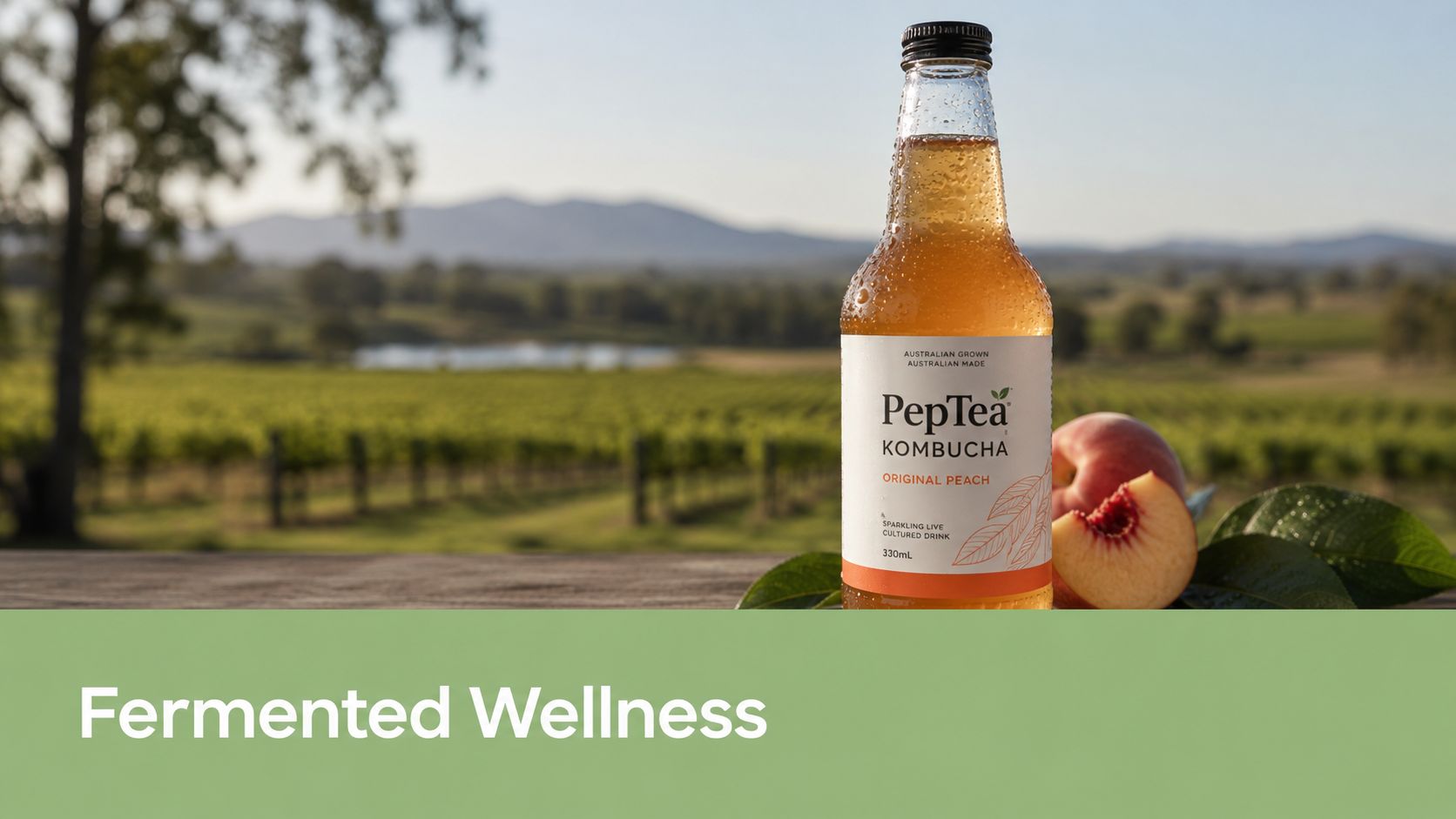 A glass bottle of PepTea peach kombucha placed on a wooden surface with a vineyard in the background.