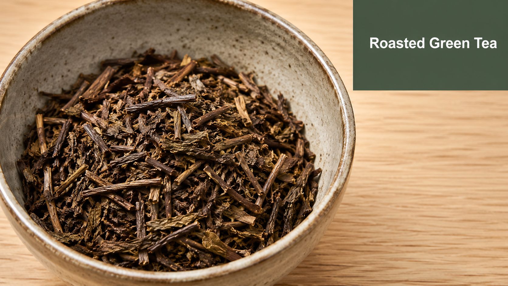 A ceramic bowl filled with roasted green tea leaves and stems on a light wooden surface.