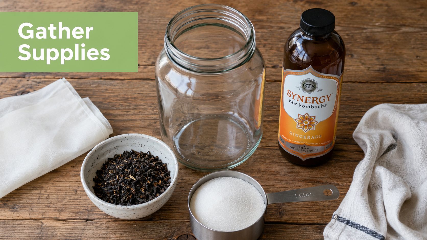 A glass jar, tea leaves, white sugar, and a bottle of kombucha arranged on a wooden table.