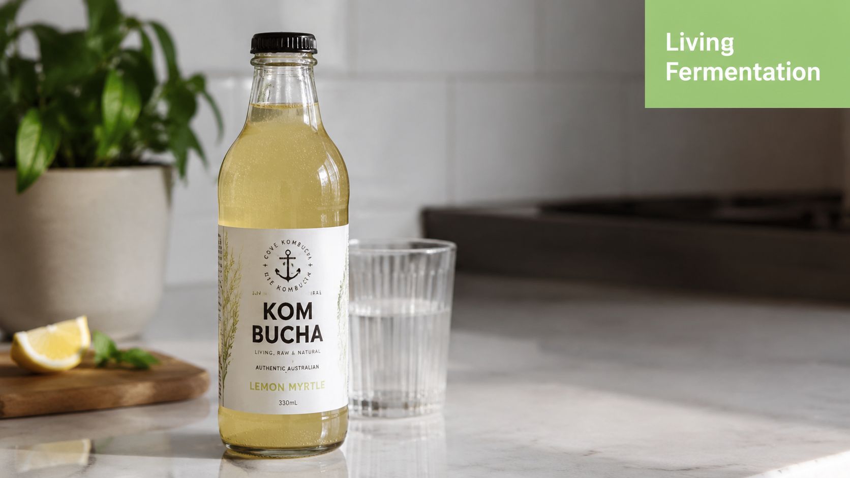 A glass bottle of Cove Kombucha Lemon Myrtle standing on a marble countertop next to a glass.
