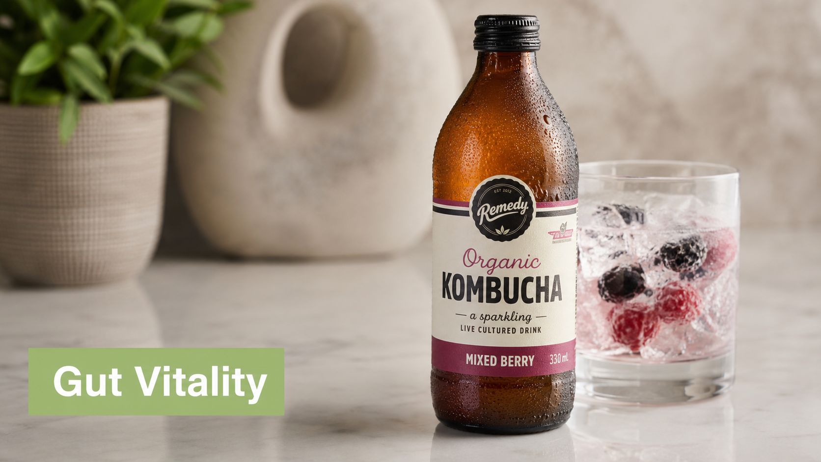 A glass bottle of Remedy organic mixed berry kombucha sitting next to a glass of iced berries.